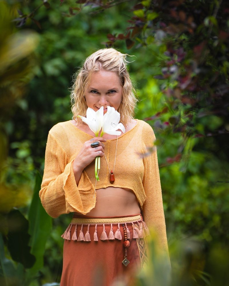 Tish Steenkamp, laughing, a light scarf over her head, forest behind her